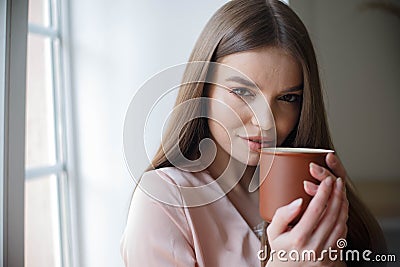 Beautiful girl is drinking coffee and smiling while sitting at the cafe Stock Photo