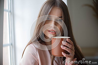 Beautiful girl is drinking coffee and smiling while sitting at the cafe Stock Photo