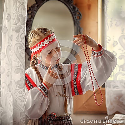 A beautiful girl in a folk costume looks at the Rowan berry beads Stock Photo