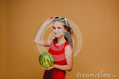 A beautiful girl in glasses and a red dress holds a watermelon in her hands Stock Photo