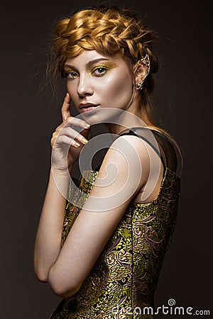 Beautiful girl in a gold dress with creative makeup and braids on her head. The beauty of the face. Stock Photo