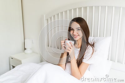 Beautiful young woman at her bedroom drinking tea in the morning. Stock Photo