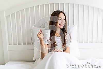 Beautiful young woman at her bedroom drinking tea in the morning. Stock Photo