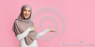 Beautiful girl in hijab pointing at something on her empty palm Stock Photo