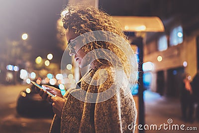 Beautiful girl hipster wearing glasses holding smart phone hands, during night walking in european vocation. Bokeh and Stock Photo