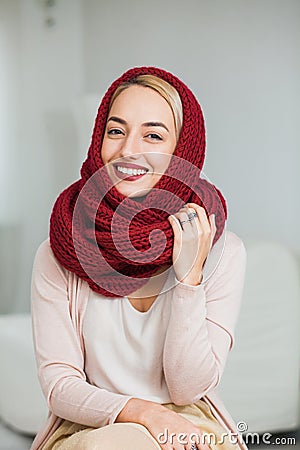 Beautiful girl knitting in cozy flat wearing casual clothes, big deep red scarf. Stock Photo