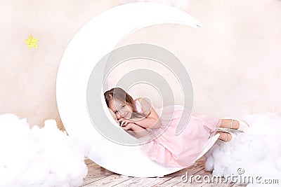 Beautiful girl lies in the studio with the decor of the moon, stars and clouds. Little girl dreaming. Sweet dreams. Little cute g Stock Photo