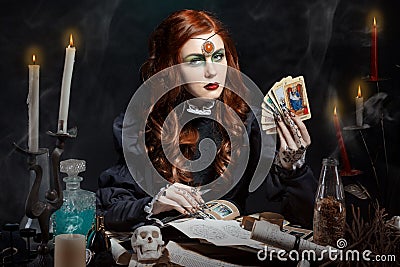 Beautiful girl with long hair mode in the image of the witch with the Tarot cards in his hands, black long false nails with bright Stock Photo