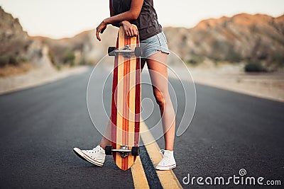 Beautiful girl with long legs enjoys a ride on a longboard at summertime. Outdoors sports activities. Stock Photo