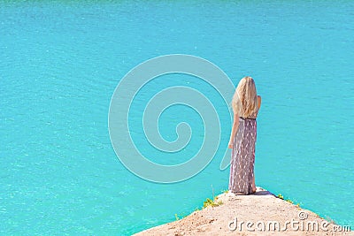 Beautiful girl with long white hair in a long dress standing on the shore of the lake with blue water in a Sunny bright day Stock Photo