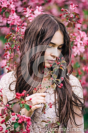 Beautiful girl near Sakura, sniffing pink flowers of the tree, looking down, closeup Stock Photo