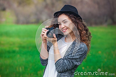 Beautiful girl-photographer with curly hair holds a camera and make a photo, spring outdoors in the park. Stock Photo