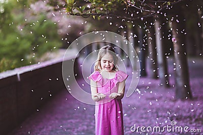 Beautiful girl in pink dress in cherry blossom park on a spring day, flower petals falling from the tree Stock Photo