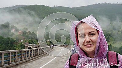 Beautiful girl with a pink sports jacket, backpack, transparent raincoat, with drops on a bridge in Montenegro Stock Photo