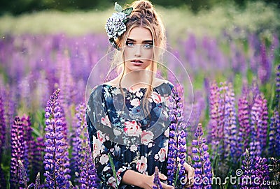 Beautiful girl in a purple lupin field with a flower on her head made of genuine leather and silk. Outdoor portrait Stock Photo