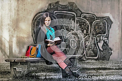 Beautiful girl reading a book in a park near a graffiti wall Editorial Stock Photo