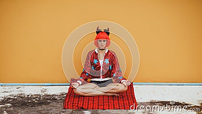 Beautiful girl in red devil costume sitting in yoga pose in anticipation of Halloween. Wears a red wig and horns. The Stock Photo