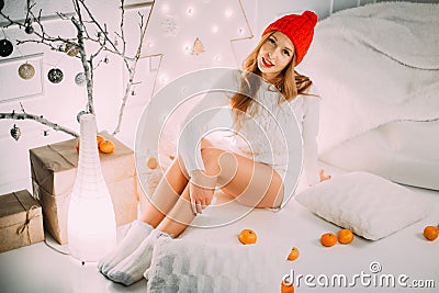 Beautiful Girl in a red hat with pompon sitting near christmas composition among mandarines and oranges. Stock Photo