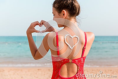 Beautiful girl in red swimsuit with sunscreen in shape of heart at the back at the beach Stock Photo