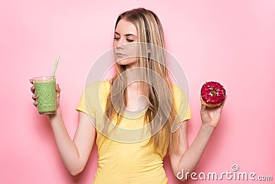 Beautiful girl is selecting between healthy green gluten-free organic smoothie and unhealthy food. Nutrition choice concept. Stock Photo