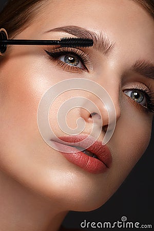 Beautiful girl with sexy lips and classic makeup with cosmetic mascara brush in hand. Beauty face. Stock Photo