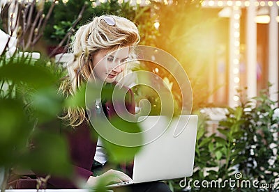Beautiful girl is sitting on a bench with a laptop in her hands on a fresh street with the city. A concept work in pleasure, Stock Photo