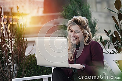 Beautiful girl is sitting on a bench with a laptop in her hands on a fresh street with the city. A concept work in pleasure, Stock Photo