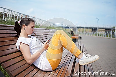 Beautiful girl sitting on bench in park with phone in hands Stock Photo