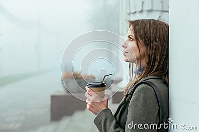 Beautiful girl sitting in foggy street holding coffe in hands and drinking through straw Stock Photo