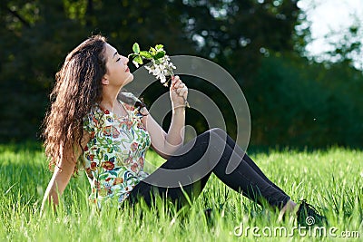 Beautiful girl sitting on a glade in the park, bright sun and shadows on the grass Stock Photo