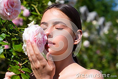 Beautiful girl smelling a rose flower in spring park. Young woman in flowering garden with roses. Beauty model with Stock Photo