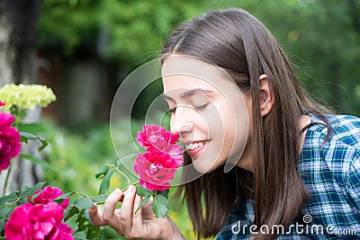 Beautiful girl smelling a rose flower in spring park. Young woman in flowering garden with roses. Beauty model with Stock Photo