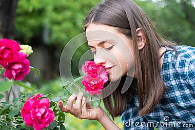 Beautiful girl smelling a rose flower in spring park. Young woman in flowering garden with roses. Beauty model with Stock Photo