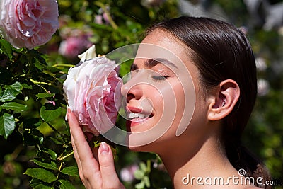 Beautiful girl smelling a rose flower in spring park. Young woman in flowering garden with roses. Beauty model with Stock Photo