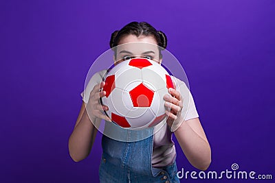 Beautiful girl with soccer ball in hands hiding half face coquette isolated blue background Stock Photo