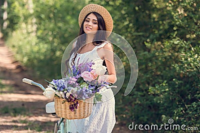 beautiful girl in straw hat and white dress posing with bicycle and flowers Stock Photo