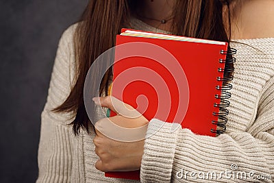 Beautiful girl student in a sweater with a red notebook on a dark backgroundred notebook in the hands of a girl Stock Photo