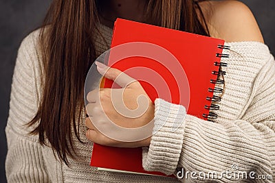 Beautiful girl student in a sweater with a red notebook on a dark backgroundred notebook in the hands of a girl Stock Photo