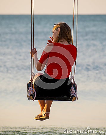 A beautiful girl swings, admires the sea, at sunrise. Editorial Stock Photo