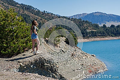 Beautiful girl in a teeshirt ans denim shorts standing at the mountain lakeshore Stock Photo