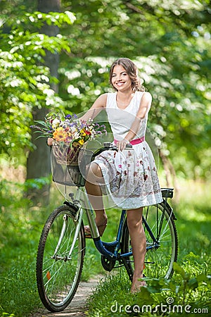 Beautiful girl wearing a nice white dress having fun in park with bicycle. Healthy outdoor lifestyle concept. Vintage scenery Stock Photo