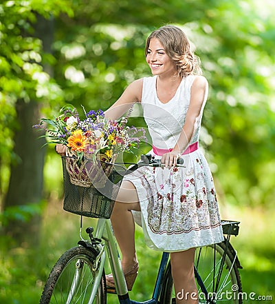 Beautiful girl wearing a nice white dress having fun in park with bicycle. Healthy outdoor lifestyle concept. Vintage scenery Stock Photo