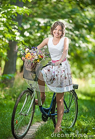 Beautiful girl wearing a nice white dress having fun in park with bicycle. Healthy outdoor lifestyle concept. Vintage scenery Stock Photo