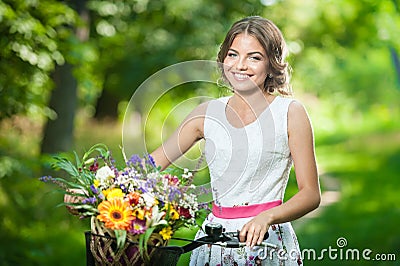 Beautiful girl wearing a nice white dress having fun in park with bicycle. Healthy outdoor lifestyle concept. Vintage scenery Stock Photo