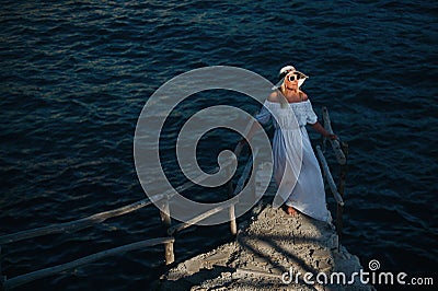 A beautiful girl in a white dress stands on the pier near the sea.Woman in Greece near the sea at sunset Stock Photo