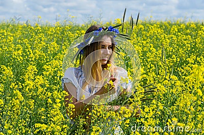 Beautiful girl in wreath of cornflowers on flowering rapeseed field Stock Photo