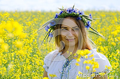 Beautiful girl in wreath of cornflowers on flowering rapeseed field Stock Photo