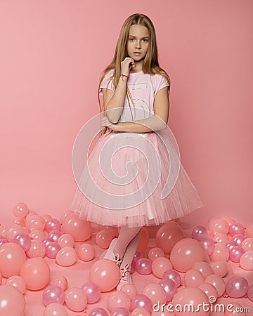 Beautiful girl 9-10 years old in pink clothes on a pink background among pink balloons. Stylish fashion photo for birthday cards, Stock Photo