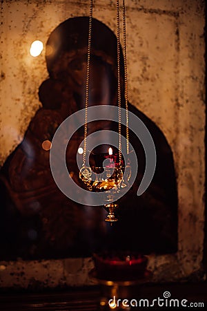 Beautiful golden figured censer thurible with burning candle hanging with chain in front of old icon of Divine Mother. Stock Photo