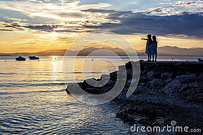 A beautiful golden sunset on the lake Garda, Italy. Silhouette of two girls Editorial Stock Photo